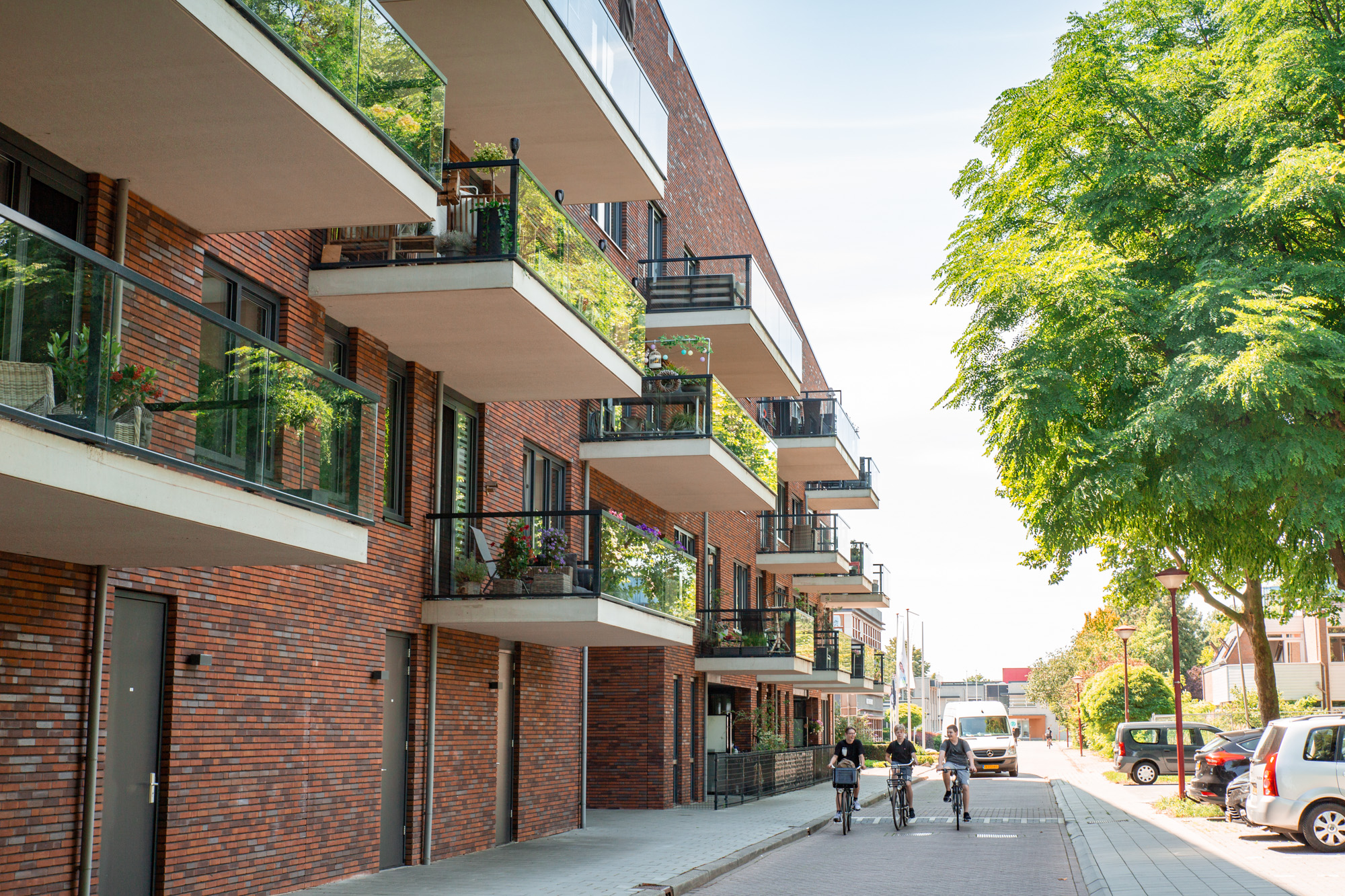 Een foto van een nieuwbouwcomplex, waaronder op straat drie kinderen de richting van de camera op komen fietsen.