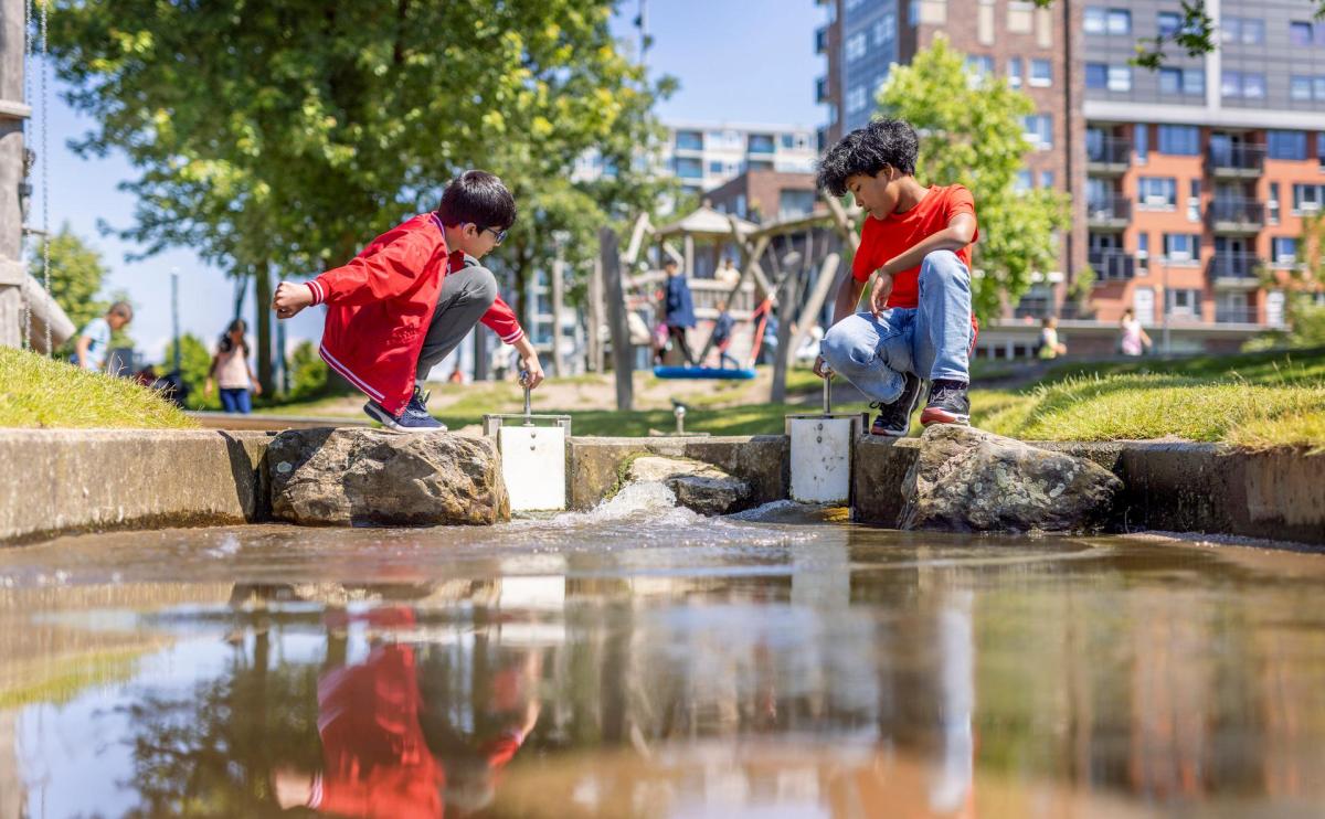 Twee jonge jongens spelen samen met water. Het is relatief warm en de foto is genomen vanaf het perspectief van de grond. We zien de jongens in het midden van het beeld naar elkaar toe zitten en lol hebben met het water.